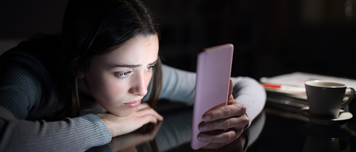 Jeune adolescente concentrée sur son smartphone dans l'obscurité, illustrant les risques de la surconnexion et l'importance de la vigilance en ligne